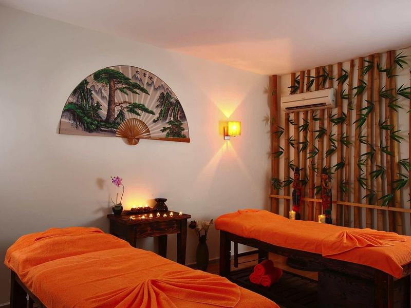 Cozy massage room with two beds, orange covers, soft lighting, and tropical decor.