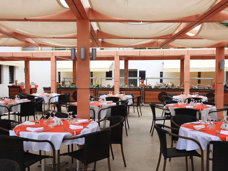 Outdoor restaurant seating with tables covered in white and orange linens under a canopy.