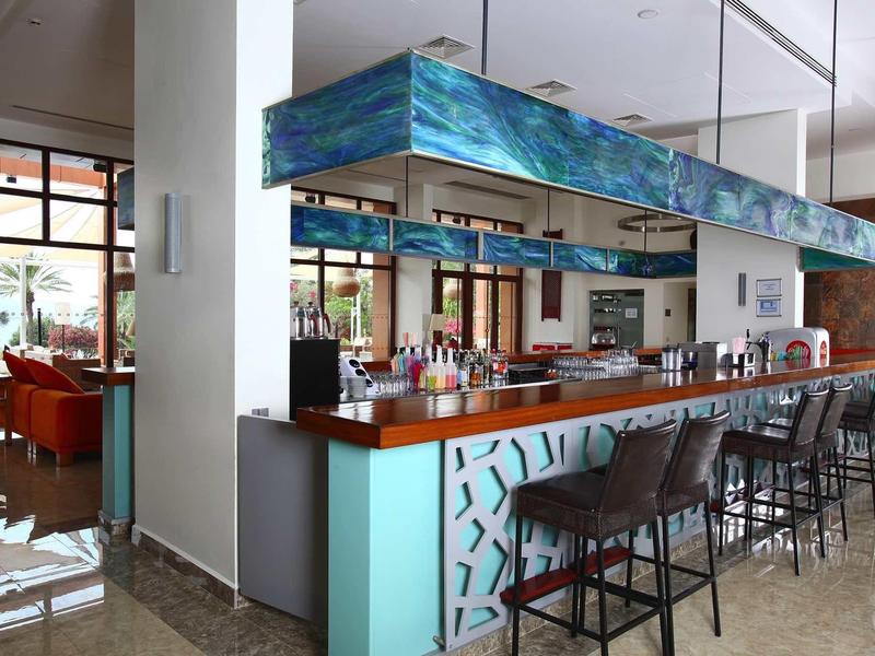 Modern hotel bar with aqua blue patterned counter and high black stools.