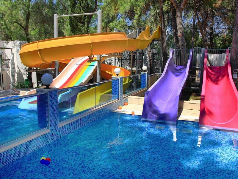 Outdoor pool with colorful water slides surrounded by trees at a hotel or resort.