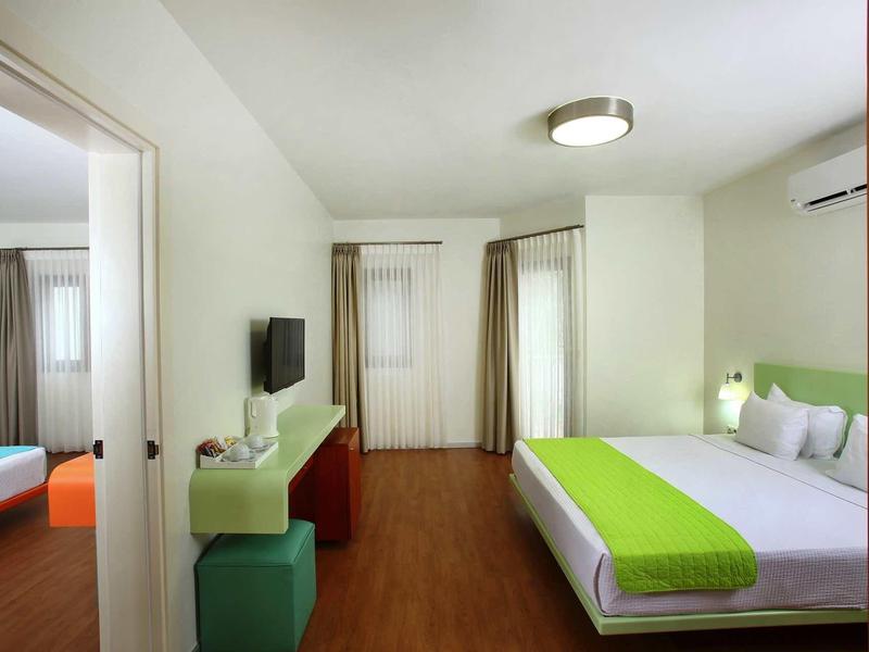 Modern hotel room with double bed, green accents, TV, and wooden flooring.