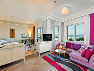 Modern hotelkamer met slaap- en woonruimte met paarse bank en groot raam.