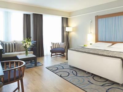 Helles Hotelzimmer mit großem Bett, Sitzbereich und Schreibtisch, modern und gemütlich eingerichtet.