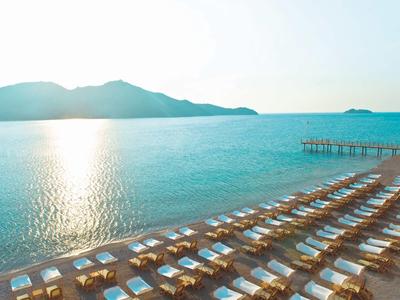 Zonsondergang boven rustige zee met ligstoelen en parasols op het zandstrand.
