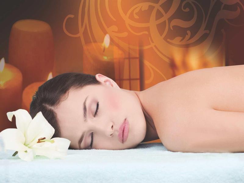 Ontspannen vrouw ligt op massagetafel met brandende kaarsen op de achtergrond.