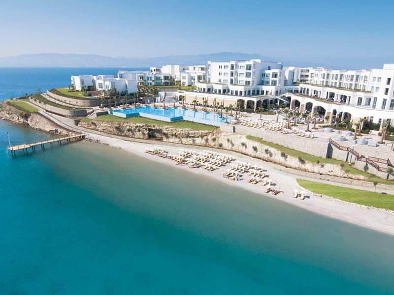 Luxe hotel met zwembad en breed zandstrand aan rustige kust onder heldere lucht.