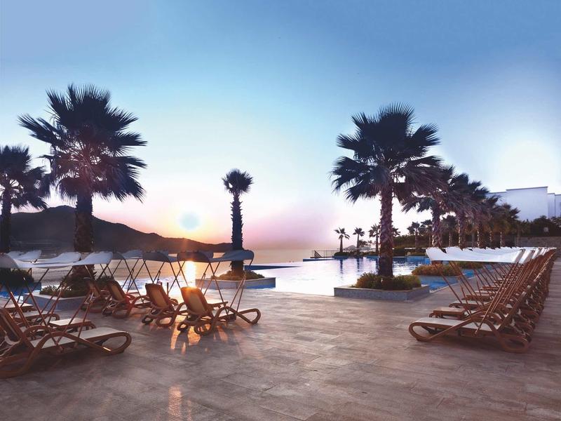 Lege ligstoelen bij het zwembad met palmbomen bij zonsondergang in een hotelresort.