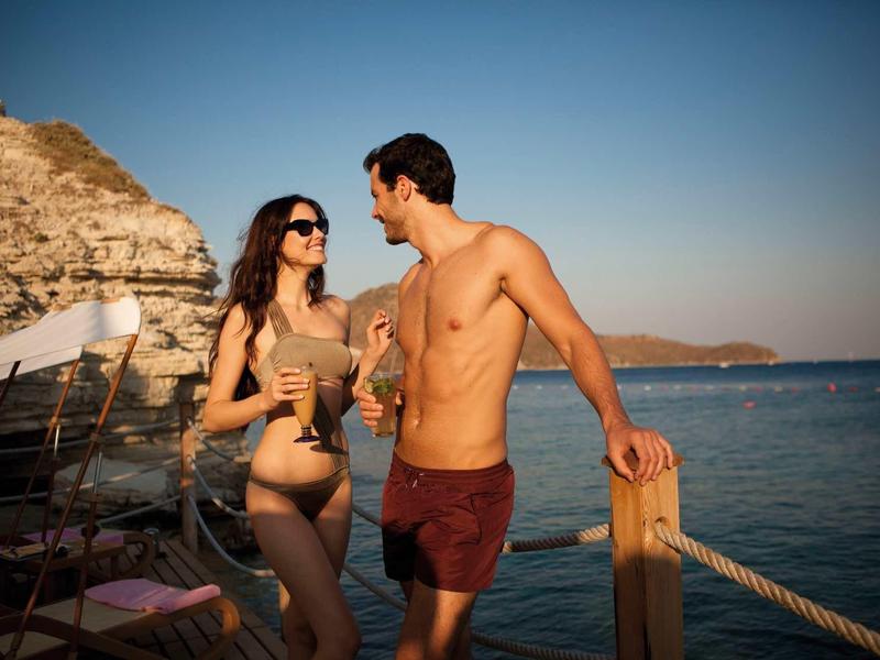 Koppel in zwemkleding praat gezellig op een houten pier bij de zee tijdens zonsondergang.