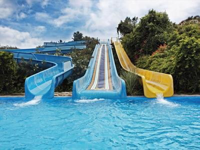 Drei bunte Wasserrutschen (blau, hellblau, gelb) enden in einem großen blauen Pool.