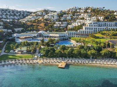 Luxuriöse Küstenanlage mit weißen Gebäuden, Pool, grünen Gärten und klaren türkisfarbenen Wasser.