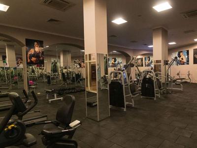 Großer Fitnessraum mit verschiedenen Trainingsgeräten und Spiegeln an den Wänden.