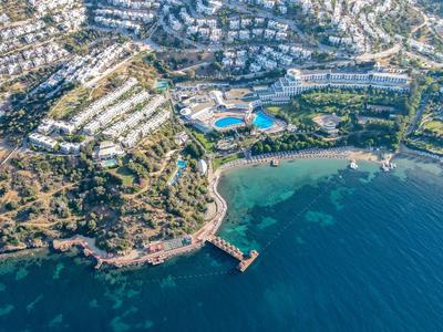 Luftaufnahme einer Küstenstadt mit weiß getünchten Häusern, Hafen, Strand und blauem Meer.