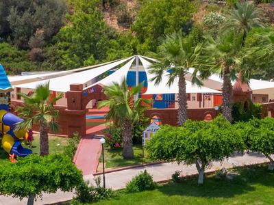 Kinder-Spielplatz mit bunten Rutschen, grünen Bäumen und Sonnensegeln in einem Park.