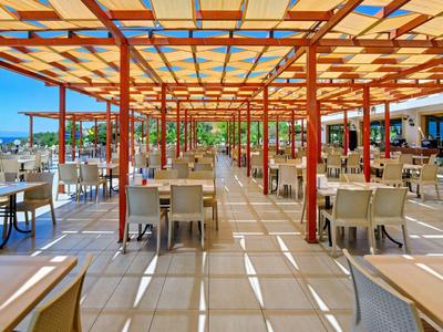 Offener Außenbereich eines Restaurants mit weißen Tischen und Stühlen unter einem Holzgitterdach.