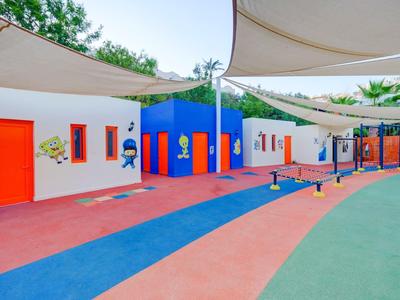 Bunte Kinderspielhalle mit verschlungenen Wegen und Sonnensegeln im Freien.