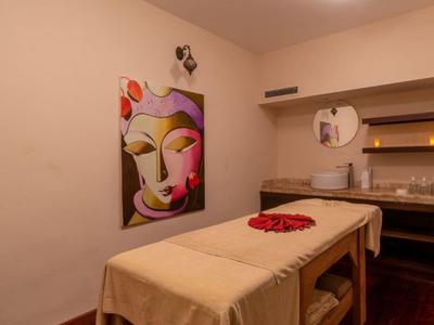 Behandlungsraum mit Massagetisch, buntem Wandbild, Regalen und warmem Licht.