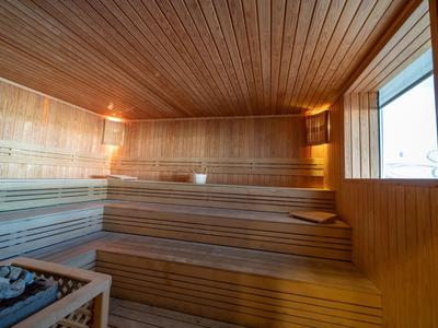 Holzsauna mit gestuften Sitzbänken, Saunaofen und großem Fenster für Tageslicht.