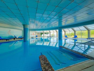 Helles Hallenbad mit blauen Fliesen, Lounge-Stühlen und großen Fenstern für Tageslicht.