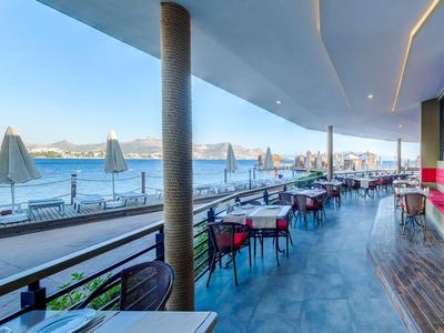Weitläufige Terrasse mit modernen Tischen und Stühlen, Überdachung, Meerblick und Sonnenschirmen.