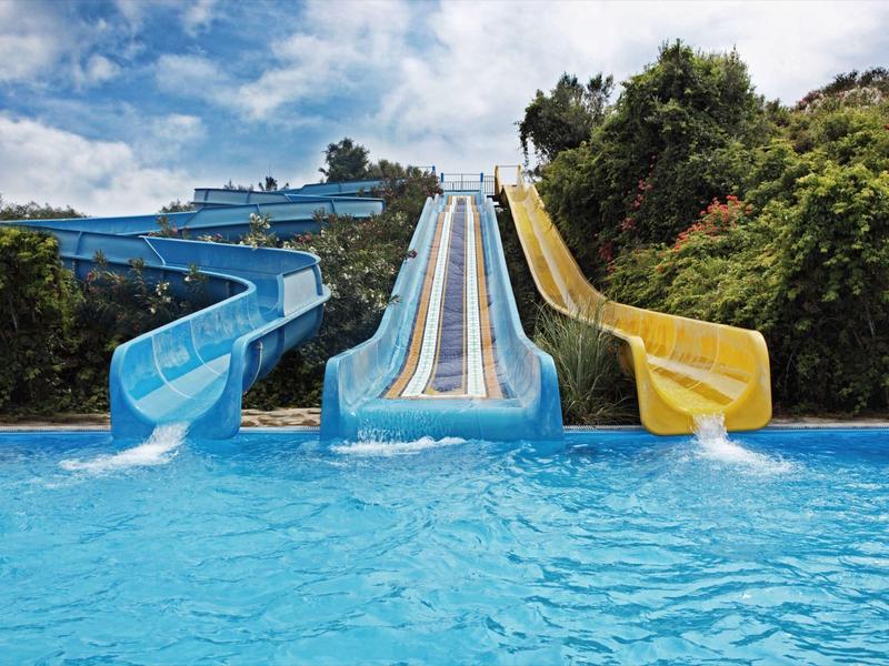 Drei bunte Wasserrutschen (blau, hellblau, gelb) enden in einem großen blauen Pool.