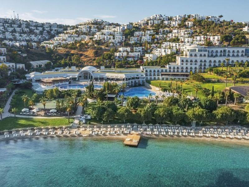 Luxuriöse Küstenanlage mit weißen Gebäuden, Pool, grünen Gärten und klaren türkisfarbenen Wasser.