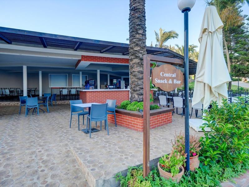 Außenbereich eines Restaurants mit blauen Stühlen, Tischen, Palmen und einem Schild "Cuisine Emirienne & Bio".