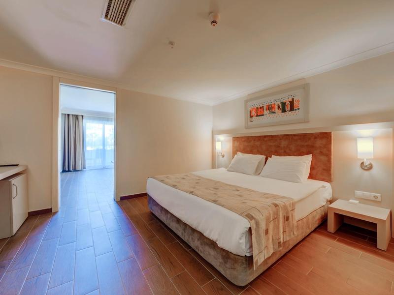 Helles Schlafzimmer mit Doppelbett, Holzboden, Nachttischen und großem Balkon.