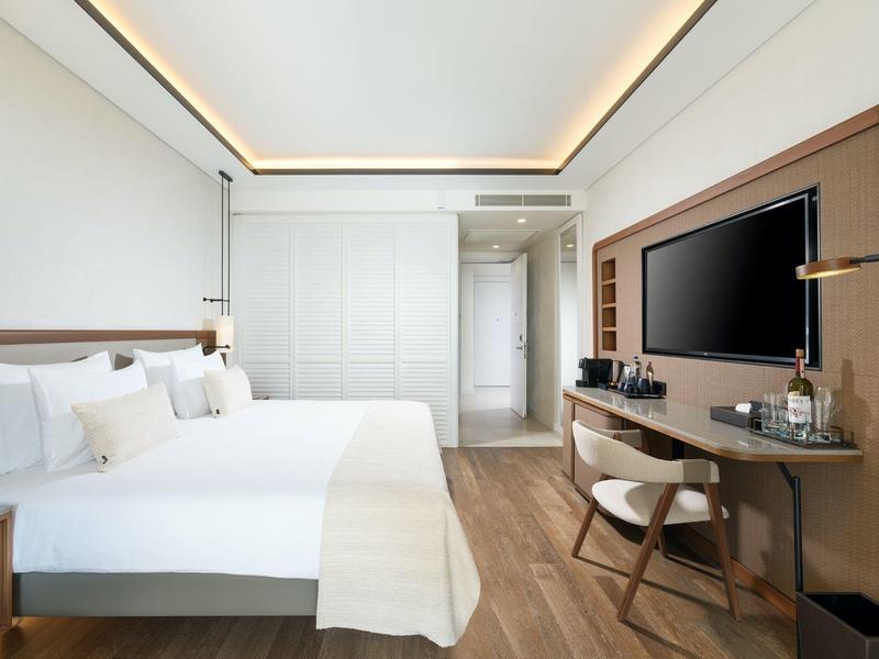 Nowoczesny, jasny pokój hotelowy z dwoma łóżkami, telewizorem, biurkiem i minimalistycznym wystrojem.