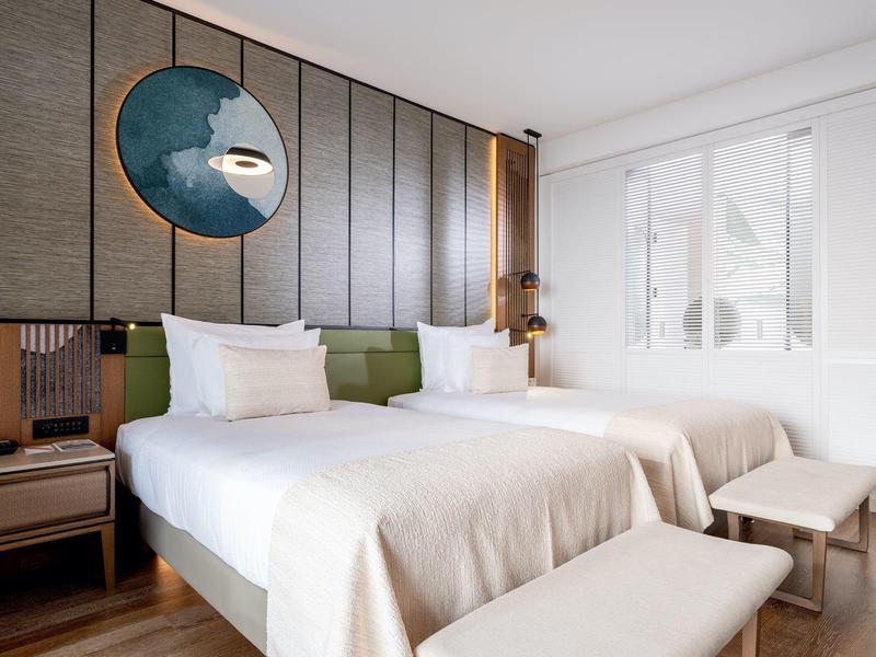 Nowoczesny pokój hotelowy z dwoma pojedynczymi łóżkami, białą pościelą i zielonymi wezgłowiami.