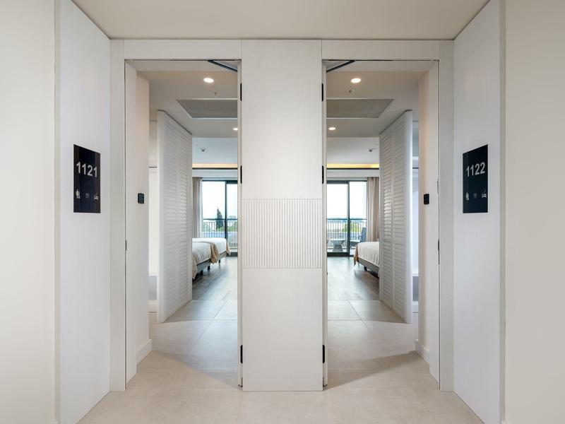 Widok na dwa otwarte drzwi do pokoi hotelowych z numerami pokoi i widokiem z okna w środku.