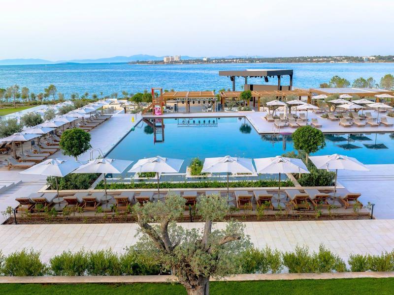 Nowoczesny basen hotelowy z leżakami i widokiem na morze w świetle dziennym.