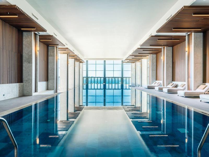 Nowoczesny basen kryty z leżakami i dużymi oknami wpuszczającymi dużo światła dziennego.