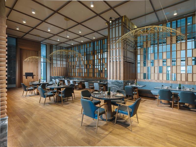 Nowoczesna część hotelu lub restauracji z niebieskimi krzesłami i drewnianą podłogą pod wysokim oknem.