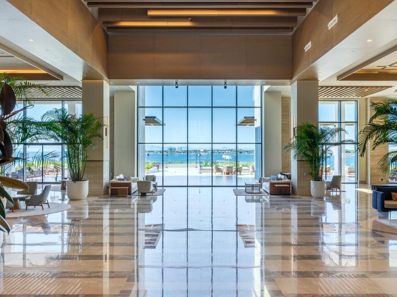 Jasna lobby hotelowa z dużymi oknami z widokiem na morze i plażę.