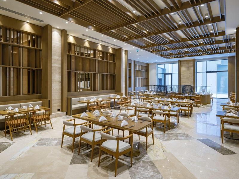 Nowoczesna jadalnia z drewnianymi stołami i dużymi jasnymi oknami.