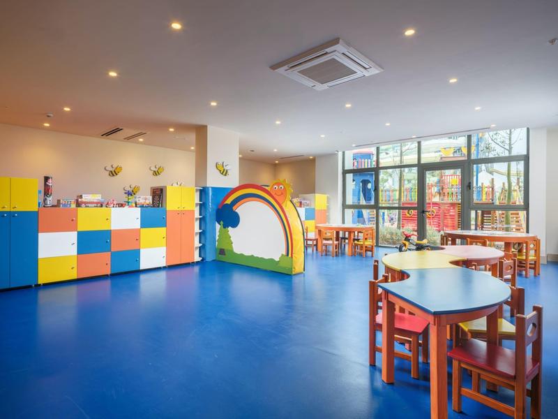 Jasny pokój zabaw dla dzieci z niebieską podłogą, kolorowymi meblami i dużymi oknami w hotelu.
