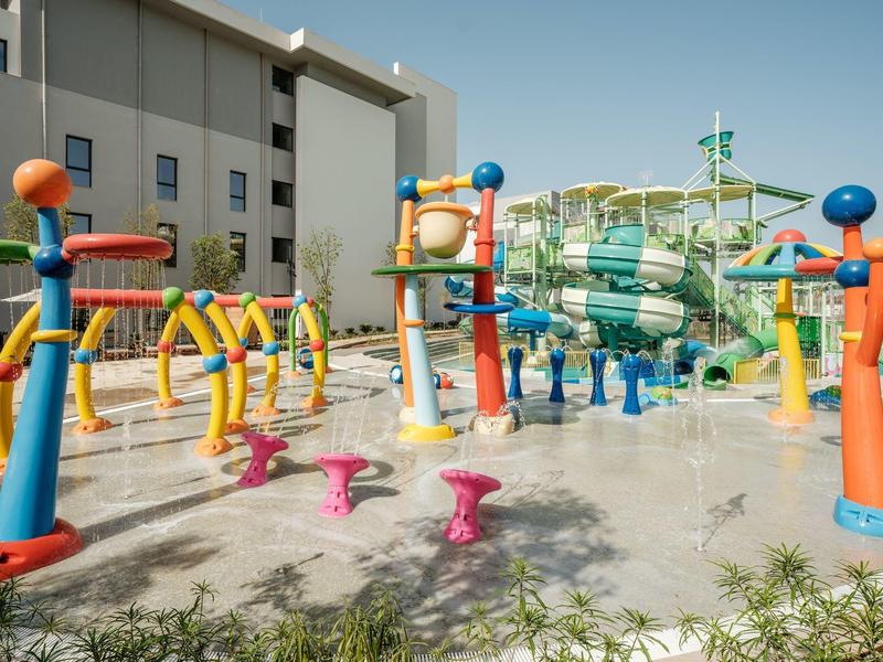 Kolorowy plac zabaw wodnych z zjeżdżalniami i spryskiwaczami obok budynku hotelu pod czystym niebem.