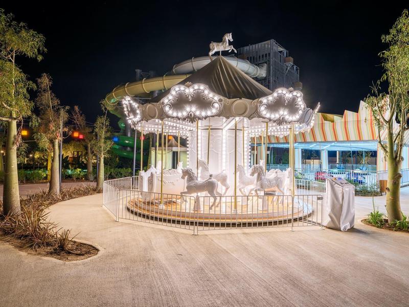 Oświetlona karuzela z białymi końmi na otwartej przestrzeni w nocy.