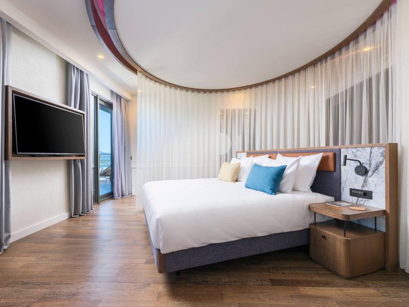 Nowoczesny pokój hotelowy z podwójnym łóżkiem, drewnianą podłogą i dużym oknem z widokiem na zewnątrz.