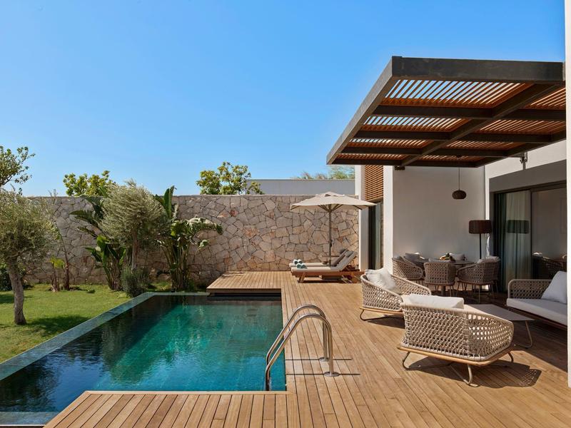 Nowoczesny basen z drewnianym tarasem i meblami wypoczynkowymi obok domu pod czystym niebem.