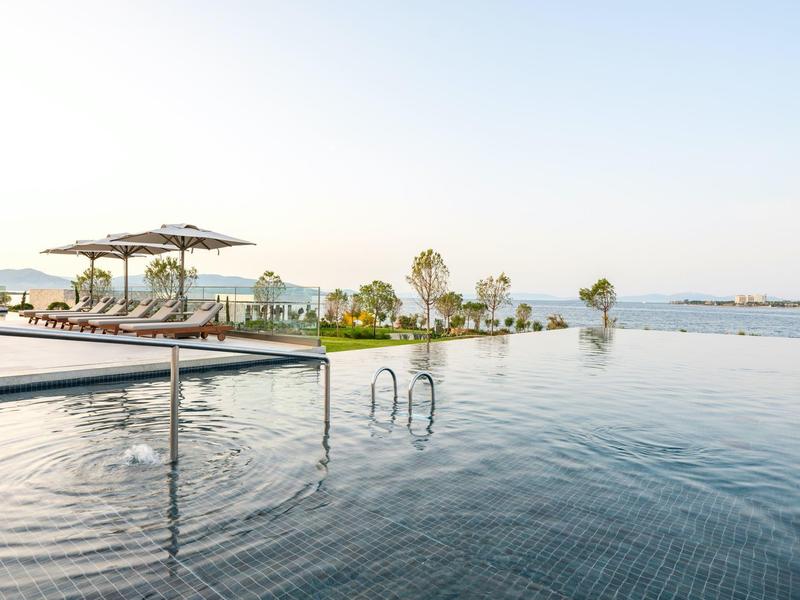 Basen typu infinity z leżakami i parasolami przy spokojnym morzu pod czystym niebem.