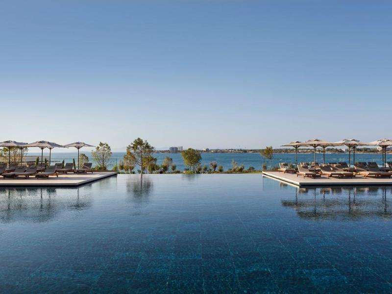 Przestronny basen hotelowy z parasolami i widokiem na morze pod czystym niebem.