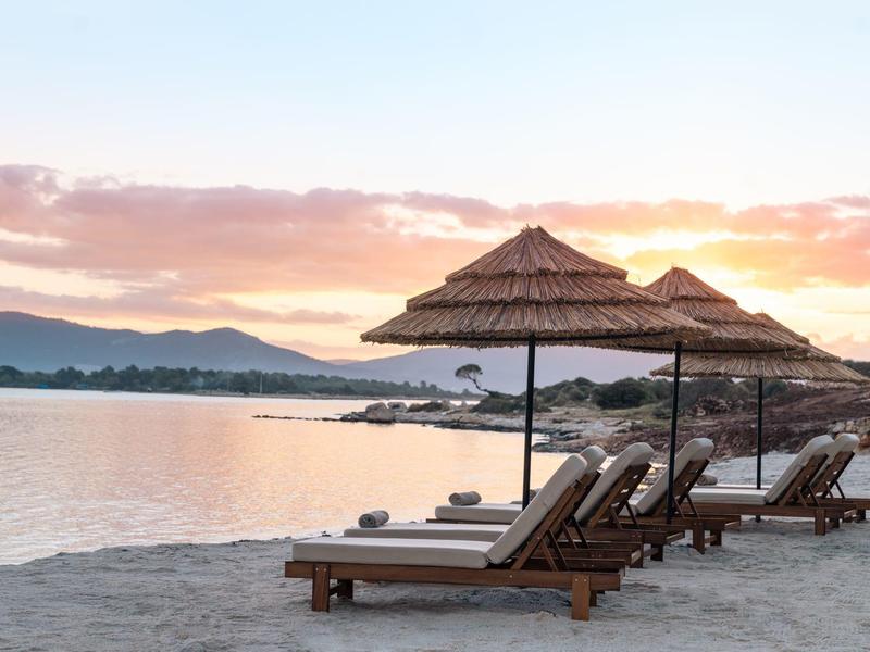 Puste leżaki z parasolami z trzciny na piaszczystej plaży o zachodzie słońca.