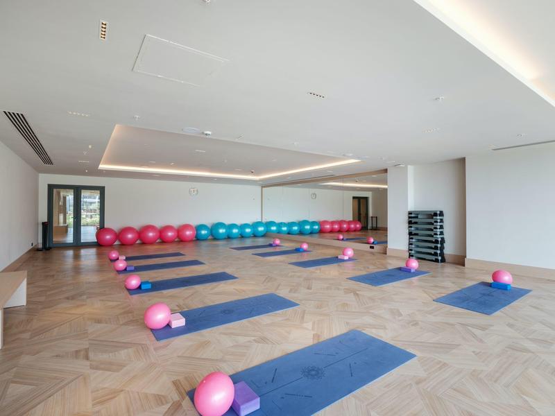 Nowoczesna sala fitness z niebieskimi matami do jogi i różowymi piłkami na drewnianej podłodze.