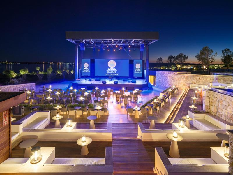 Nowoczesna przestrzeń zewnętrzna z sceną, miejscami do siedzenia i ciepłym oświetleniem na wieczorne wydarzenia