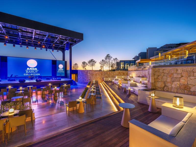 Taras hotelowy na zewnątrz o zmierzchu z miejscami do siedzenia i dużym ekranem pod czystym niebem.