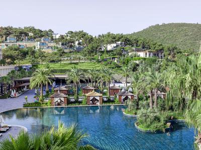 Resort met groot zwembad, ligstoelen en weelderig groen onder een heldere lucht.