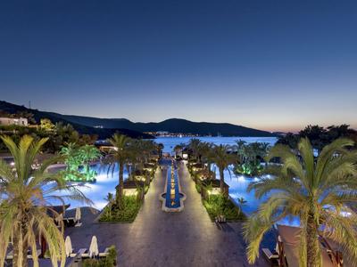 Nachtelijke resortzwembad met palmbomen en uitzicht op zee op de achtergrond.