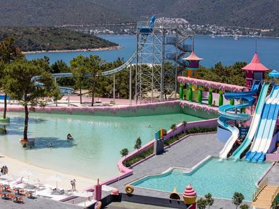 Waterpark met glijbanen, zwembad en strandgebied voor een bebost kustlandschap.