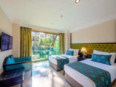 Jasny pokój hotelowy z dwoma pojedynczymi łóżkami, zielonym wystrojem i widokiem na ogród.